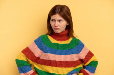 Sarı arka planda izole edilmiş genç bir İngiliz kadın kafası karışmış, şüpheli ve güvensiz hissediyor..