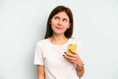 Mavi arka planda cep telefonu tutan genç İngiliz kadın hedeflere ve amaçlara ulaşma hayali kuruyor.
