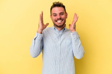 Sarı arka planda izole edilmiş genç beyaz adam yüksek sesle gülüyor ve elini göğsüne koyuyor..