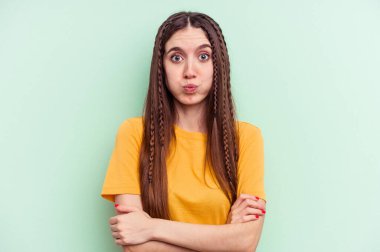 Yeşil arka planda izole edilmiş genç beyaz kadın yanakları patlatıyor, yorgun bir ifadesi var. Yüz ifadesi kavramı.