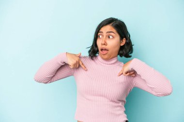 Mavi arka planda izole edilmiş genç Latin kadın parmağını göstererek şaşırdı, geniş bir gülümsemeyle..