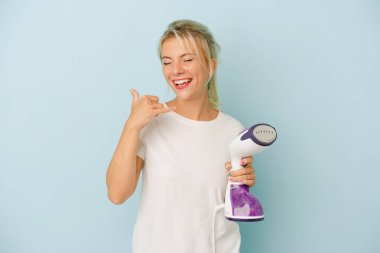 Mavi arka planda dikey demir tutan genç Rus kadın parmaklarıyla bir cep telefonu hareketi gösteriyor..