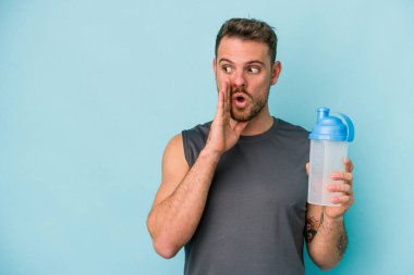 Mavi arka planda izole edilmiş milkshake içen genç beyaz adam gizli bir sıcak fren haberi veriyor ve yan tarafa bakıyor.