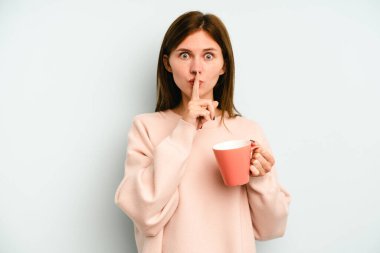 Mavi arka planda bir kupa tutan genç bir İngiliz kadın ya sır saklıyor ya da sessizlik istiyor..