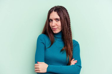 Genç beyaz kadın yeşil arka planda izole edilmiş şüpheli, belirsiz, seni muayene ediyor..