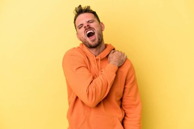 Sarı arka planda izole edilmiş, omuz ağrısı olan genç beyaz bir adam..