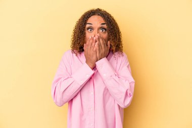 Sarı arka planda izole edilmiş genç Latin transseksüel kadın şok olmuş, ağzı ellerle kaplanmış, yeni bir şey keşfetmeye hevesli..
