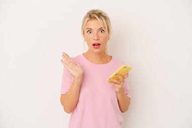 Beyaz arka planda cep telefonu tutan genç Rus kadın şaşırdı ve şok oldu..