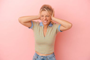 Pembe arka planda izole edilmiş genç bir Rus kadın kulakları elleriyle kapatıyor..