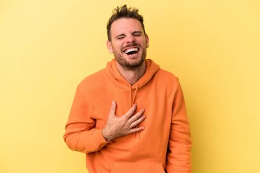 Sarı arka planda izole edilmiş genç beyaz adam yüksek sesle gülüyor ve elini göğsüne koyuyor..