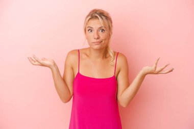 Pembe arka planda izole edilmiş genç bir Rus kadın şüpheye düşüp omuz silkiyor..