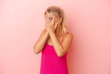 Pembe arka planda izole edilmiş genç Rus kadın parmaklarının arasından korkmuş ve gergin bir şekilde göz kırpıyor..