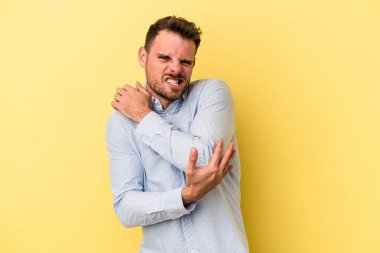 Genç beyaz adam sarı arka planda izole edilmiş dirsek masajı yapıyor, kötü bir hareketin ardından acı çekiyor..