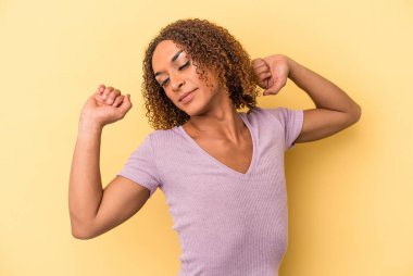 Sarı arka planda izole edilmiş genç Latin transseksüel kadın kollarını uzatıyor, rahat pozisyonda..