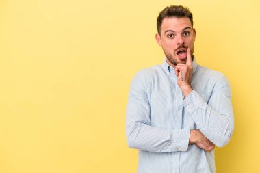 Sarı arka planda izole edilmiş genç beyaz adam şüpheli ve şüpheci bir ifadeyle yana bakıyor..