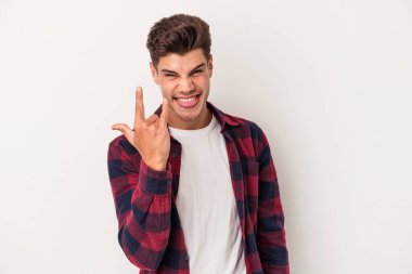 Beyaz arka planda izole edilmiş genç beyaz bir adam parmaklarıyla kaya hareketi gösteriyor.