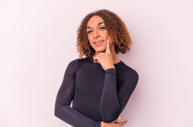 Genç Latin transseksüel kadın pembe arka planda izole edilmiş mutlu ve kendinden emin gülümsüyor, elleriyle çenesine dokunuyor..