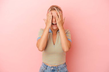 Pembe arka planda izole edilmiş genç Rus kadın yüzünün yarısını avuç içiyle kaplayarak eğleniyor..