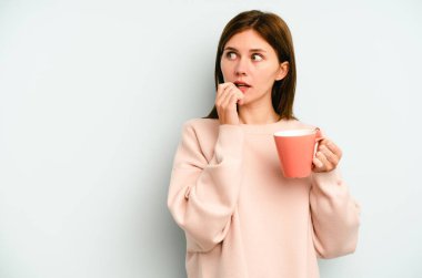 Mavi arka planda izole edilmiş bir kupa tutan genç İngiliz kadın rahatlamış fotokopi odasına bakan bir şey düşünüyor..
