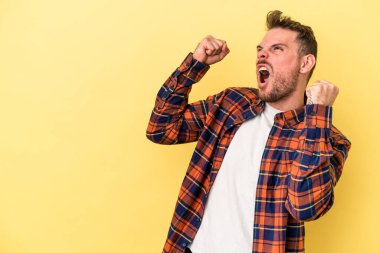 Sarı arka planda izole edilmiş genç beyaz adam zaferden sonra yumruğunu kaldırıyor, kazanan konsept..