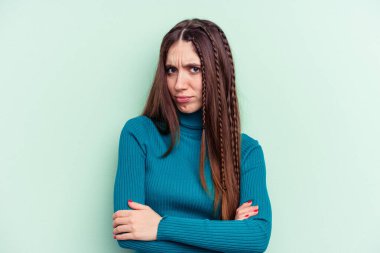 Genç beyaz kadın, yeşil arka planda izole edilmiş. Mutsuz, iğneleyici bir ifadeyle kameraya bakıyor..