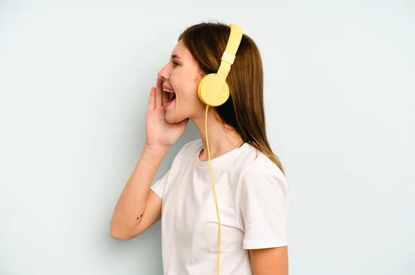 Jovem Inglesa Ouvindo Música Isolada Fundo Azul Gritando Segurando Palma — Fotografia de Stock