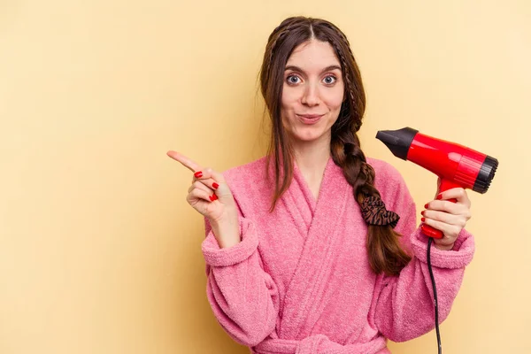 Young Woman Holding Hairdryer Isolated Yellow Background Smiling Pointing Aside — Stock Photo, Image
