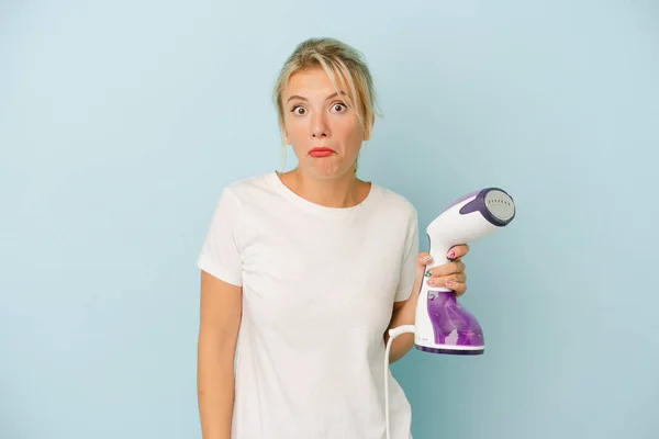 Young Russian Woman Holding Vertical Iron Isolated Blue Background Shrugs — Stock Photo, Image