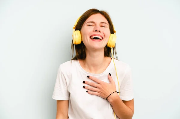若い英語の女性は青の背景に隔離された音楽を聞いて笑います大声で手を保つ胸 — ストック写真