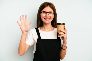 Restoran garsonu elinde kahve tutan kadın mavi arka planda izole edilmiş gülümseyen beş numarayı parmaklarıyla gösteriyor..