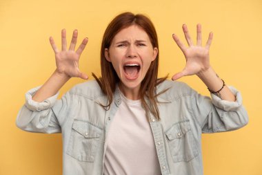 Sarı arka planda izole edilmiş genç bir İngiliz kadın pençelerini kedi taklidi yaparken gösteriyor, agresif bir hareket..