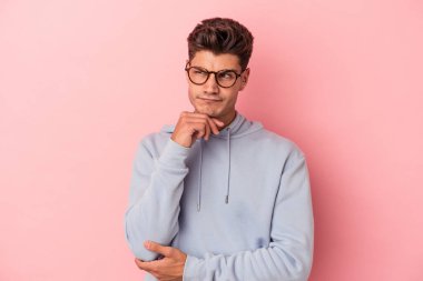 Pembe arka planda izole edilmiş genç beyaz adam şüpheli ve şüpheci bir ifadeyle yana bakıyor..