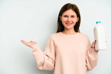 Mavi arka planda bir şişe süt tutan genç İngiliz kadın bir avuç içinde fotokopi alanı ve belinde başka bir el tutan.