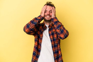 Sarı arka planda izole edilmiş genç beyaz adam ellerini başının üstünde tutarak neşe içinde gülüyor. Mutluluk kavramı.