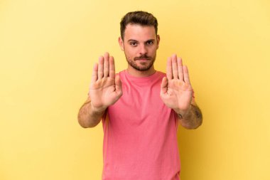 Sarı arka planda izole edilmiş genç beyaz adam elini uzatmış, dur işareti göstererek seni engelliyor..