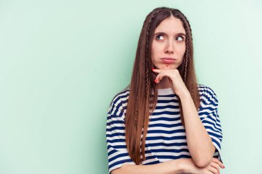 Yeşil arka planda izole edilmiş genç beyaz kadın şüpheli ve şüpheci bir ifadeyle yana bakıyor..