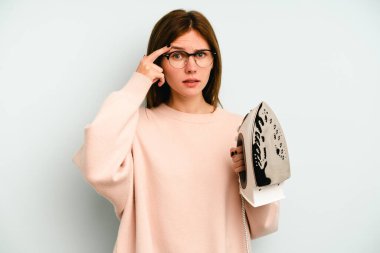 Mavi arka planda demir tutan genç İngiliz kadın işaret parmağıyla bir hayal kırıklığı gösteriyor..