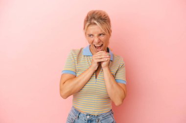 Pembe arka planda izole edilmiş genç bir Rus kadın ellerini çenesinin altında tutuyor ve mutlu bir şekilde yan tarafa bakıyor..