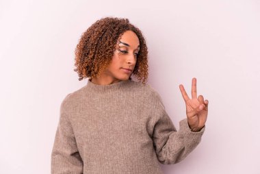 Genç Latin transseksüel kadın pembe arka planda izole edilmiş neşeli ve tasasız parmaklarıyla barış sembolü gösteriyor..