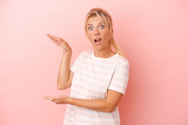 Pembe arka planda izole edilmiş genç bir Rus kadın elleri arasında bir kopya alanı tutarken şok olmuş ve hayrete düşmüş..