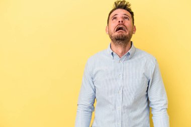 Sarı arka planda izole edilmiş genç beyaz bir adam çok kızgın, öfkeli, hayal kırıklığına uğramış diye bağırıyor..