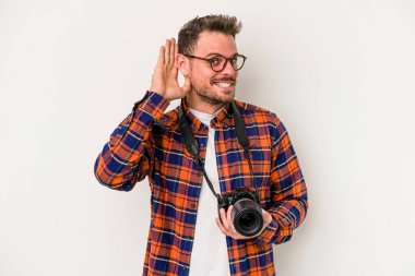 Beyaz arka planda izole edilmiş genç beyaz fotoğrafçı bir dedikoduyu dinlemeye çalışıyor..