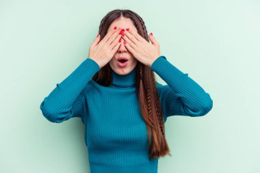 Yeşil arka planda izole edilmiş genç beyaz kadın elleriyle gözlerini kapatmaktan korkuyor..
