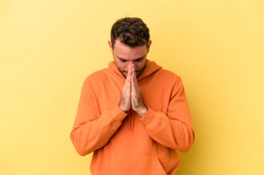 Kafkasyalı genç adam sarı arka planda izole edilmiş dua ediyor, bağlılık gösteriyor, dindar biri ilahi ilham arıyor..