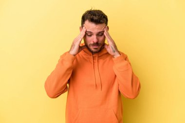 Kafkasyalı genç adam sarı arka planda izole edilmiş, başı ağrıyor, yüzüne dokunuyor..