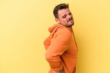 Sarı arka planda izole edilmiş beyaz bir adam sırt ağrısı çekiyor..
