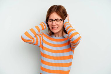 Mavi arka planda izole edilmiş genç bir İngiliz kadın kulakları elleriyle kapatıyor..