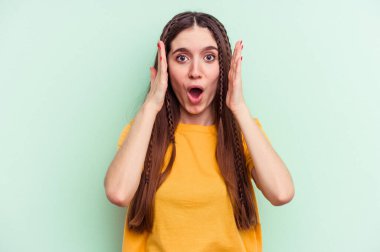 Yeşil arka planda izole edilmiş genç beyaz kadın şaşırdı ve şok oldu..