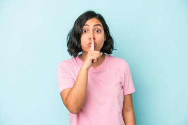Mavi arka planda izole edilmiş genç Latin bir kadın ya sır saklıyor ya da sessizlik istiyor..