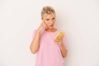 Elinde cep telefonu olan genç bir Rus kadın beyaz arka planda izole edilmiş. Şakağı işaret ediyor, düşünüyor ve bir göreve odaklanıyor..